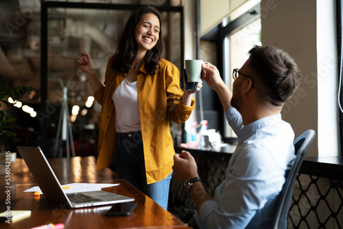 Colleagues laughing in office. Businesswoman and businessman drinking coffee