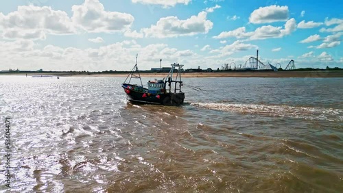 Aerial, video footage of a fishing trawler, boat, ship sailing into the midday sun, trawling for fish off the Lincolnshire coast, near Skegness in the UK. showing boat pulling nets across a sandy sea photo