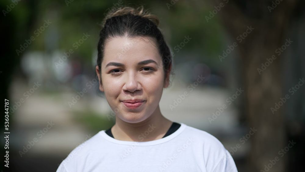 Happy young woman portrait face closeup standing outside looking at camera. Casual female person in 20s stands outdoors Happy young woman portrait face closeup standing outside looking at camera. Casual female person in 20s stands outdoors