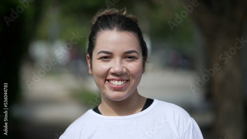 Happy young woman portrait face closeup standing outside looking at camera. Casual female person in 20s stands outdoors