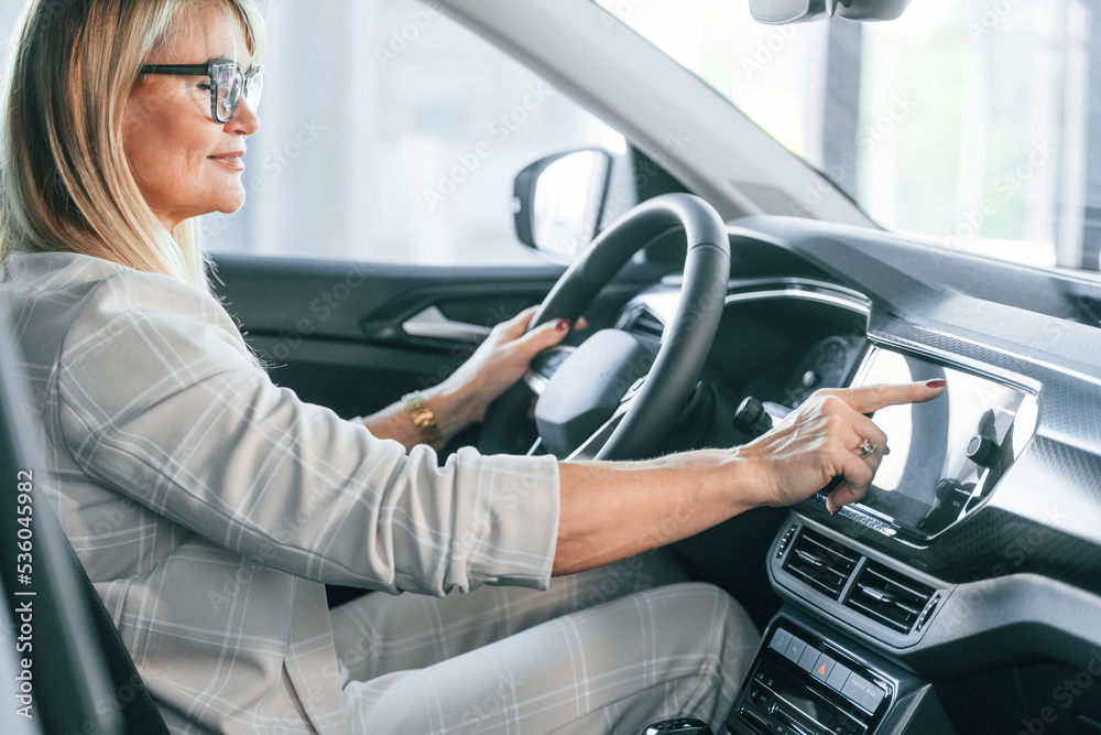 Sitting in the automobile. Woman in white formal clothes is in the car dealership Sitting in the automobile. Woman in white formal clothes is in the car dealership