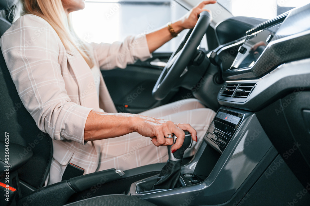 Sitting in the automobile. Woman in white formal clothes is in the car dealership