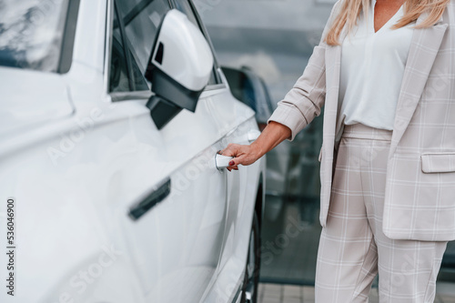Close up view of hand opening the door. Woman in white formal clothes is in the car dealership © standret