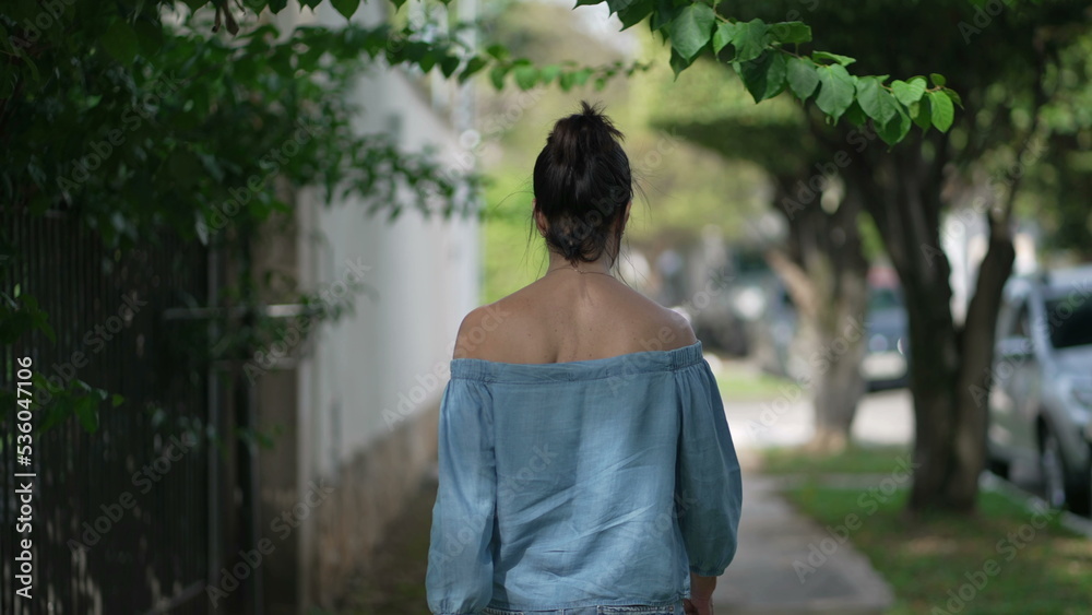 Back of mature woman walking in green city street. One middle aged 50s female person walks in sidewalk in contemplation 2 Back of mature woman walking in green city street. One middle aged 50s female person walks in sidewalk in contemplation 2