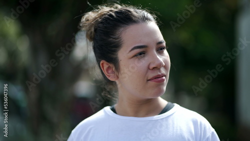 A casual Brazilian girl walking in city street. One pensive 20s woman walks in slow motion outdoors