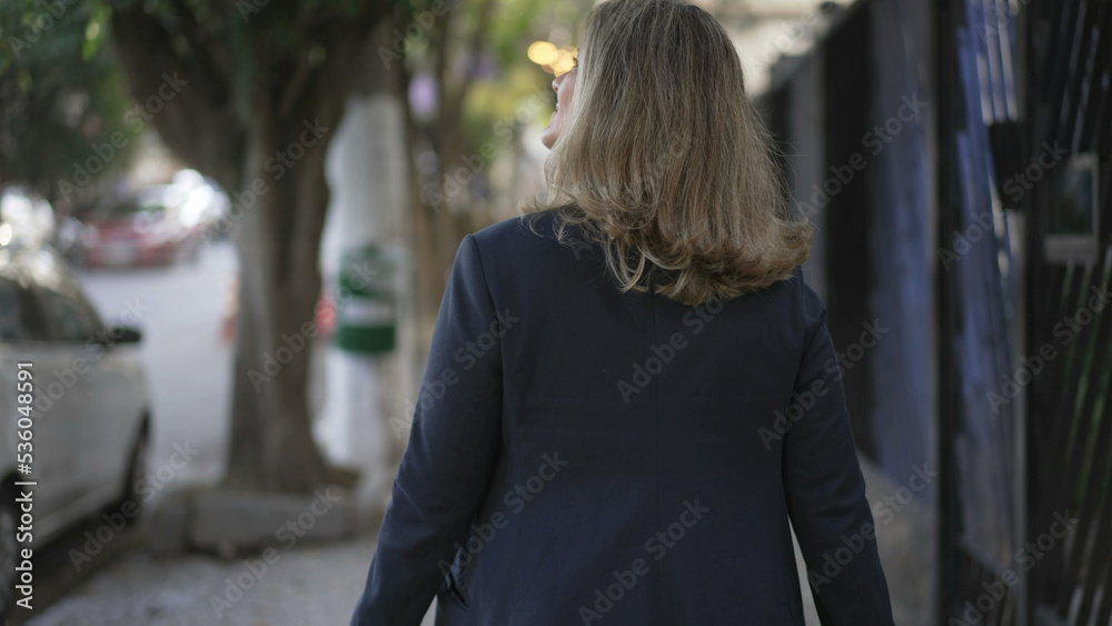 Fototapeta premium Back of person walking in city street. Contemplative woman walks outdoors in urban sidewalk