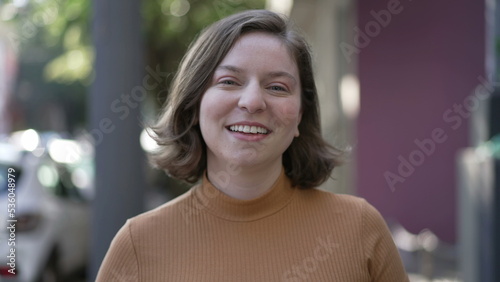 Portrait of a joyful woman walking toward camera. Tracking motion shot of person coming forward smiling. Happy millennial 20s girl in city sidewalk