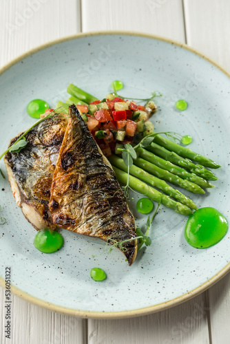 Halved grilled sea bass fish with fresh asparagus and vegetables on plate