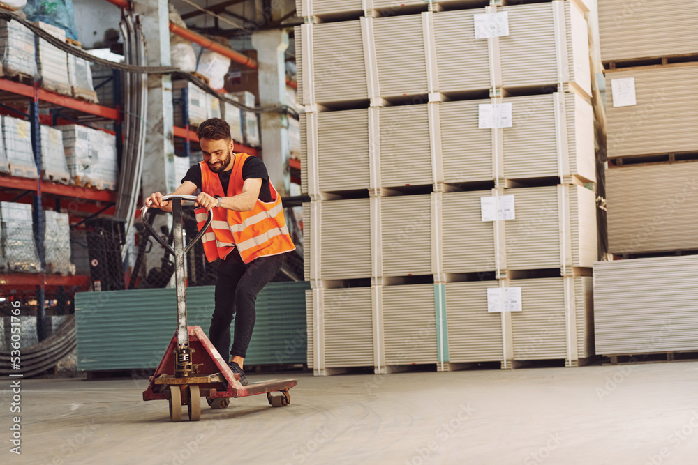 Riding the platform trolley. Storage worker is in the warehouse with bunch of products Riding the platform trolley. Storage worker is in the warehouse with bunch of products