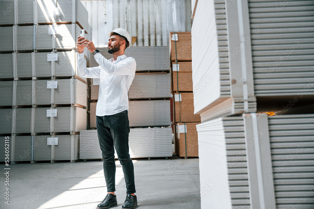 Using phone. Storage worker is in the warehouse with bunch of products Using phone. Storage worker is in the warehouse with bunch of products