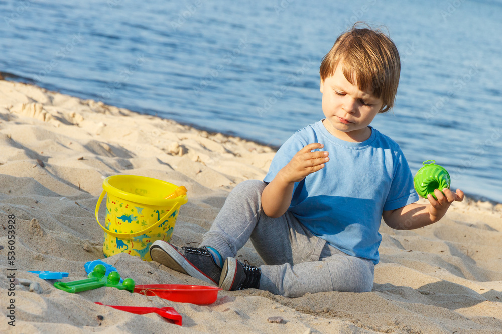 Baby boy playing with sand on summer beach. Vacation time and child development concept Baby boy playing with sand on summer beach. Vacation time and child development concept