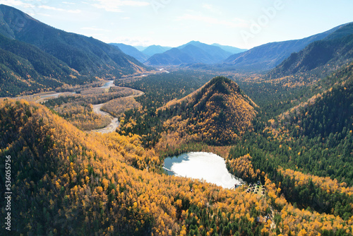 Beautiful autumn landscape from the air. A lake in the autumn forest, mountains covered with yellow leaves.