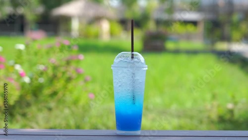 Fresh blue hawaii syrup and ice cube with soda and for summer time on wooden table in green garden tree background.