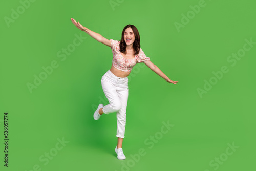 Full length photo of sweet good mood girl with curly hairdo wear white pants blouse running rejoice isolated on green color background