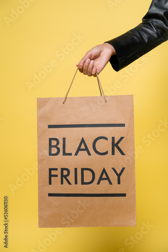 cropped view of african american woman holding black friday shopping bag on yellow.