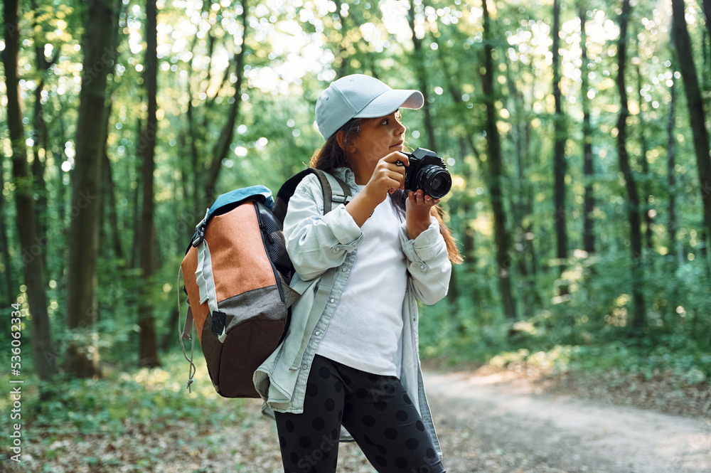 Standing and holding camera in hands. Girl is in the forest at summer day time discovering new places