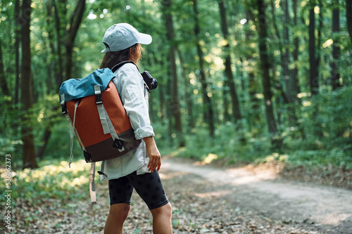 With hiking backpack. Girl is in the forest at summer day time discovering new places