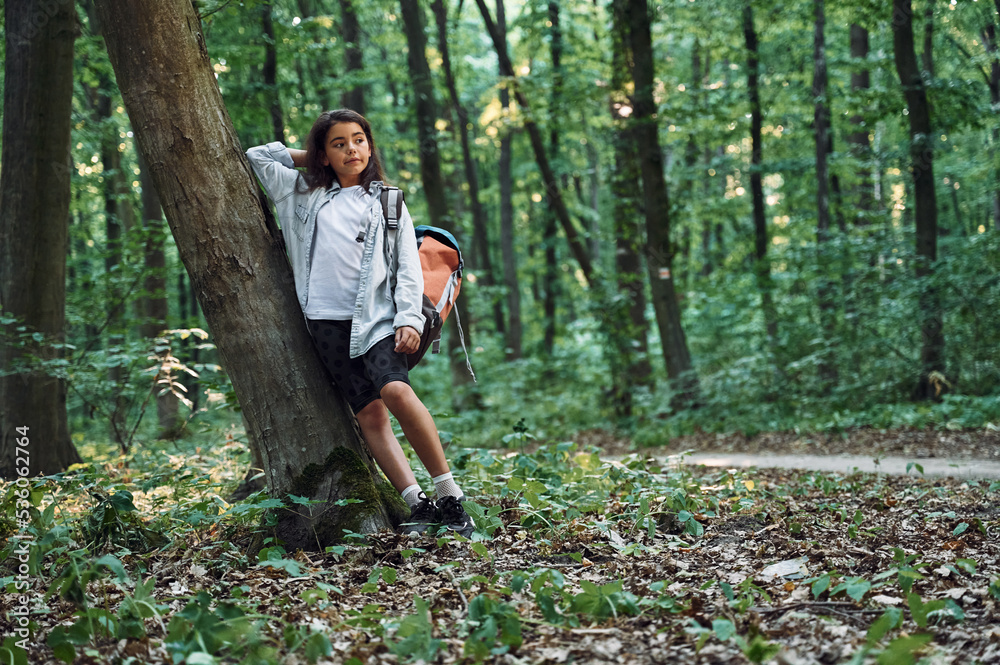 Leaning on the tree. Girl is in the forest at summer day time discovering new places