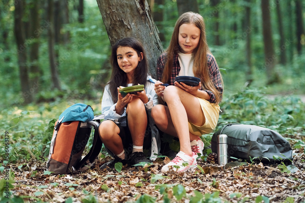 Eating by using plastic forks and plates. Two girls is in the forest having a leisure activity, discovering new places