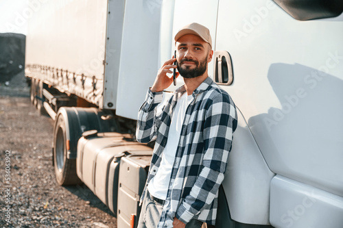 Talking by phone. Young truck driver is with his vehicle at daytime photo