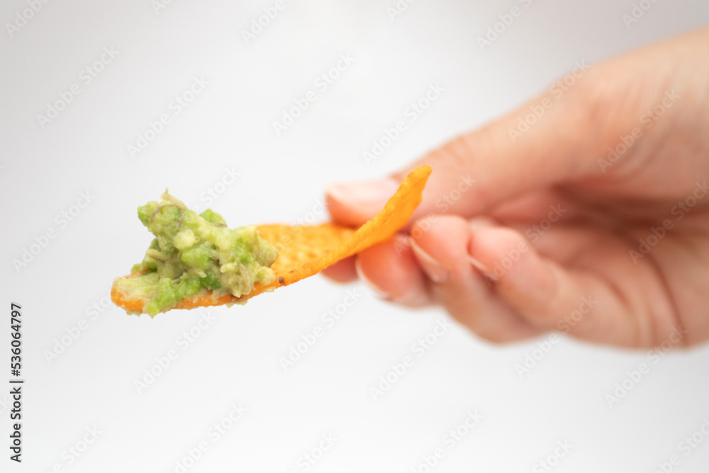 Hand with a nachos chip and guacamole dip Hand with a nachos chip and guacamole dip