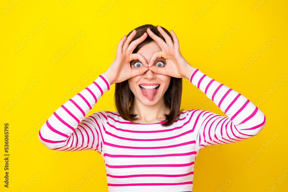 Photo portrait of pretty young lady tongue out fingers show okey glasses dressed stylish striped outfit isolated on yellow color background Photo portrait of pretty young lady tongue out fingers show okey glasses dressed stylish striped outfit isolated on yellow color background