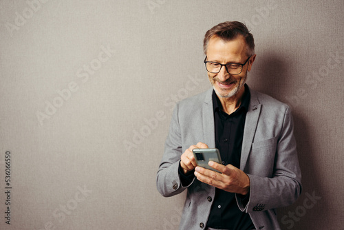 smiling bearded man looks at screen of mobile phone, isolated over brown backgro Fototapeta