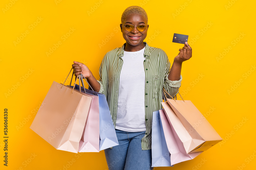 Photo of attractive nice girl arm hold showing debit plastic card boutique packages isolated on yellow color background Photo of attractive nice girl arm hold showing debit plastic card boutique packages isolated on yellow color background