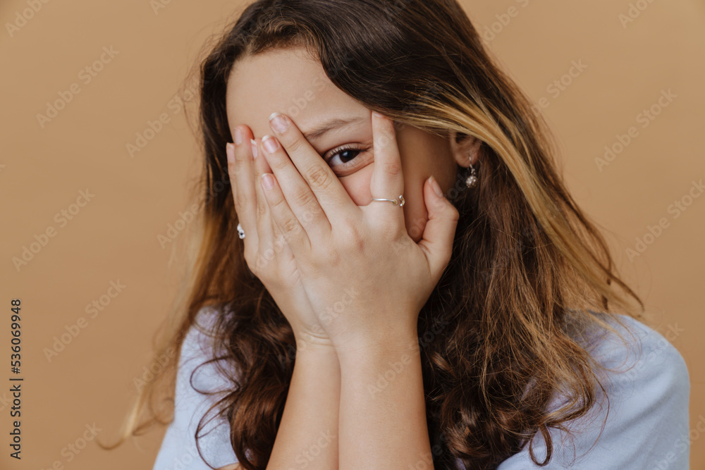 Young beautiful long-haired girl peeking out behind her fingers Young beautiful long-haired girl peeking out behind her fingers