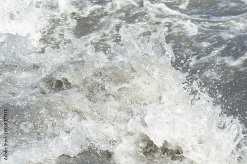Close-up white water of the mountain stream in a summer day. White and grey foam of waves and drops of water