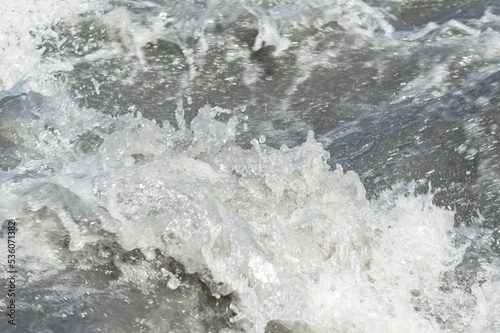 Close-up white water of the mountain stream in a summer day. White and grey foam of waves and drops of water