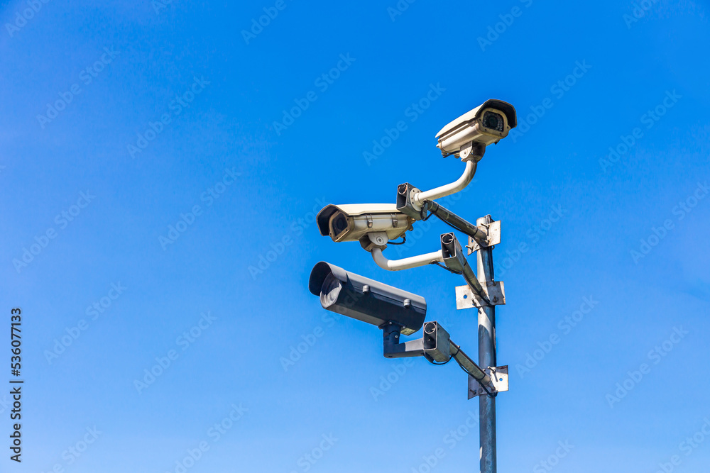Old security camera or CCTV sits on a pole with a sky background.