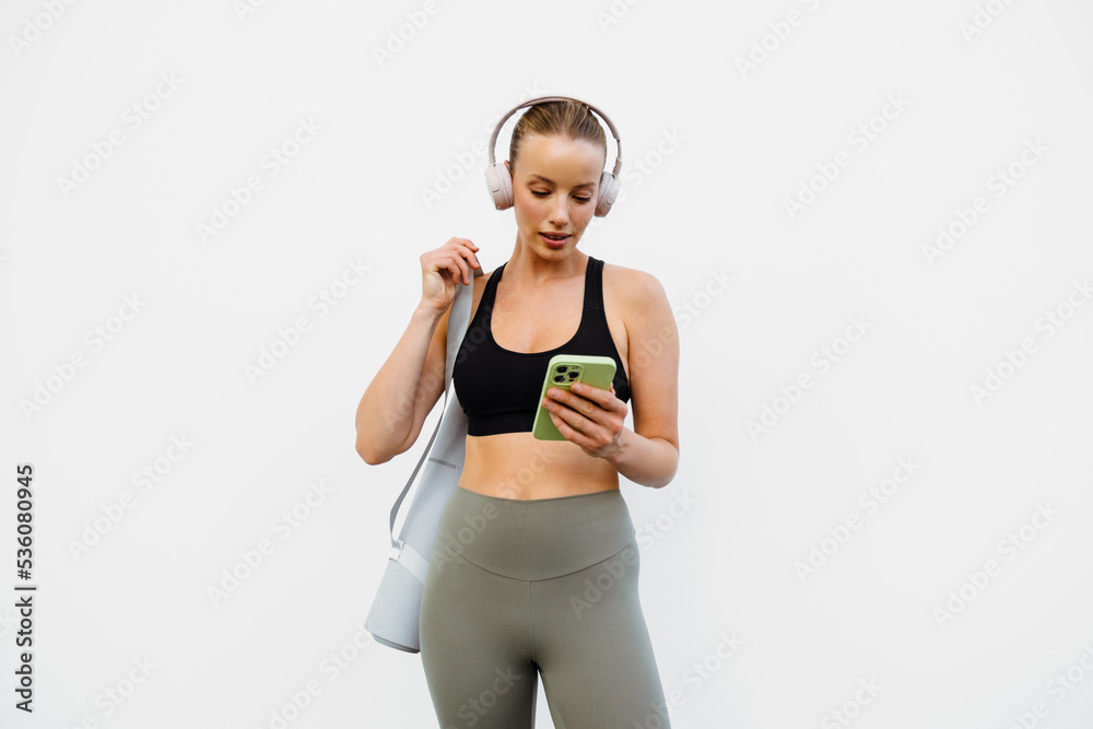 White young woman in headphones using mobile phone after yoga practice White young woman in headphones using mobile phone after yoga practice