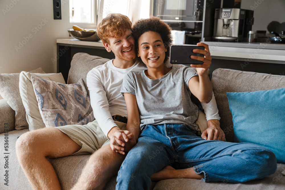 Young multinational couple taking selfie photo on cellphone at home