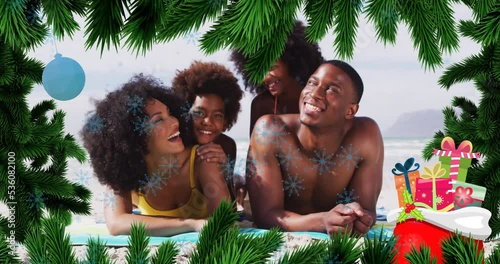 Animation of fir tree frame and snowflakes over happy african americna family on beach photo