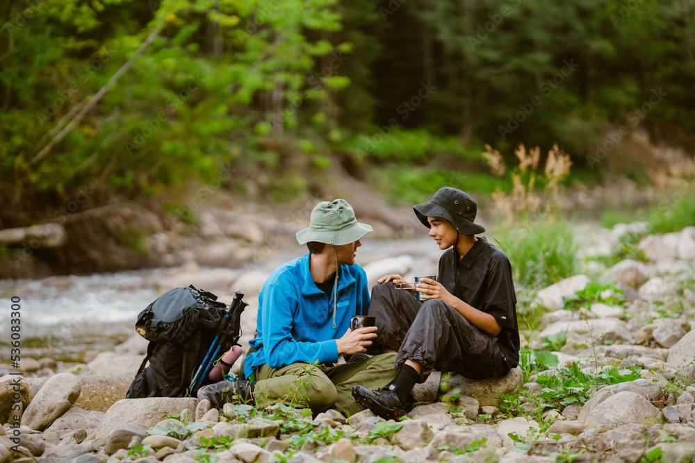 White young travelers resting by river while hiking together in nature