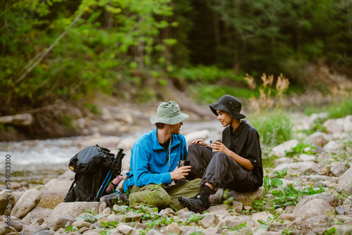 White young travelers resting by river while hiking together in nature © Drobot Dean