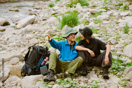 White young travelers resting by river while hiking together in nature