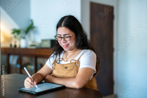 Portrait asian freelance people business female wearing glasses stylish hipste Draw or taking note on digital tablet with electronic pen for browsing internet, chatting and blogging in coffee shop. photo