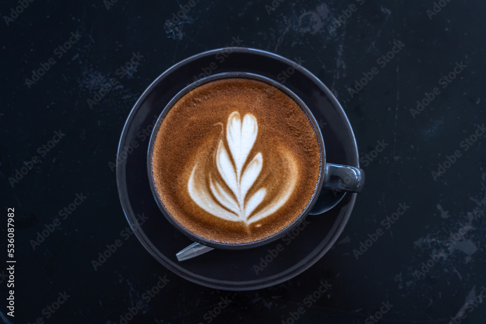 Hot coffee latte with latte art milk foam in cup mug on black wood desk on top view. As breakfast In a coffee shop at the cafe,during business work concept