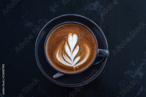 Hot coffee latte with latte art milk foam in cup mug on black wood desk on top view. As breakfast In a coffee shop at the cafe,during business work concept