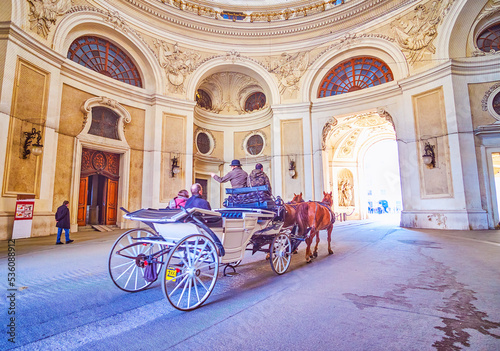 The horse-drawn carriages ride through the passageway of Michaelertor of Hofburg palace, Vienna, Austria photo