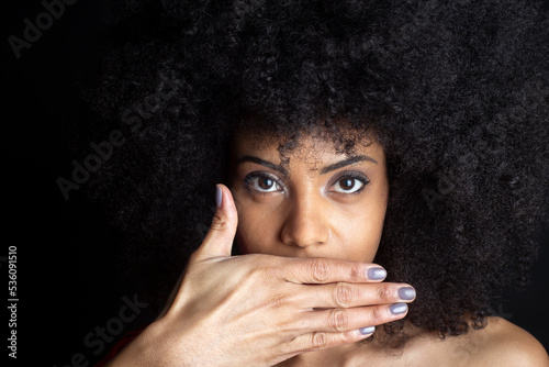 Shy ethnic woman covering mouth on black background