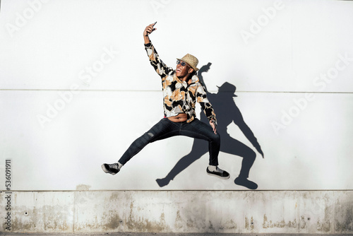 Black man jumping and taking selfie near wall photo