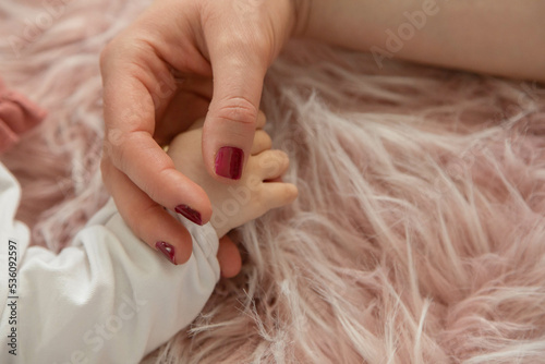 Little baby girl i holding mother's hand on a pink fur rug.