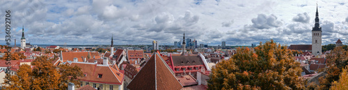 Bird view of historic city center of Tallinn, Estonia and modern town behind. Autumn trees, towers and orange tile roofs of ancient, medieval houses under cloudy overcast Northern sky with clouds.