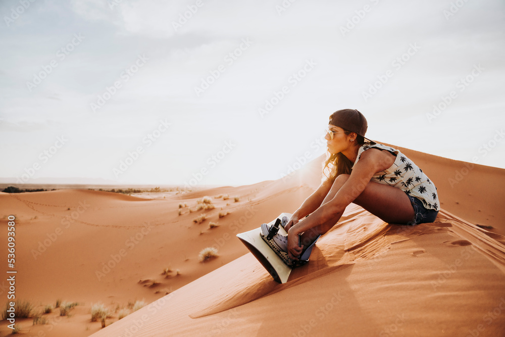 Young woman sitting on sand ready for sandboarding Young woman sitting on sand ready for sandboarding