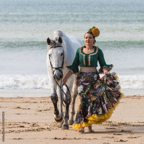 Woman in gypsy flamenco dress strolling with horse on ocean coast