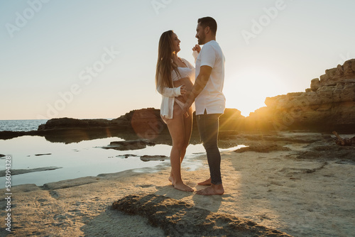 Pregnant couple standing near sea at sunrise