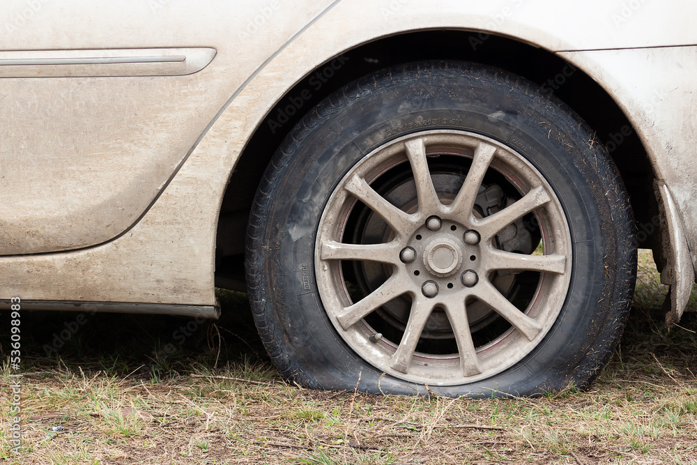 Flat tire on a white car on grass. Car wheel flat tire off road. Waiting repair help. Side view.
